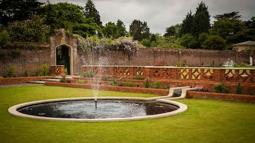Shendish Manor Hotel - lawn with a statement piece water fetaure. Brick walls with planting and gorgeous wisteria.